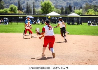 First base softball player throws the softball to the second base player while the opponent runs to second base