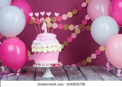 First birthday cake with a unit on a pink background with balls and paper garland.