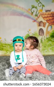 First Birthday Cute Baby Boy Wearing A St. Patrick's Day Hat And His Sister. Cartoon Fairy House On Background