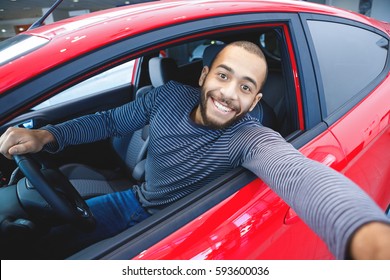 First Car Pic. Handsome Young African Man Smiling Making A Selfie Sitting In His New Car At The Dealership. Buyer Consumerism Lifestyle Travel Concept