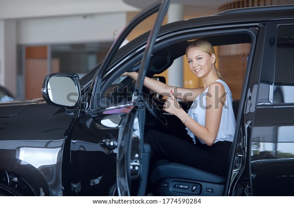 First car purchase a beautiful and happy\
girl gets into a luxury car at a car\
dealership