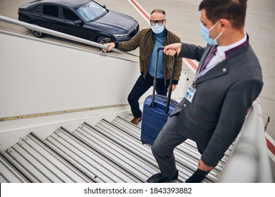 First Class Male Passenger In A Protective Mask Ascending The Aircraft Steps Accompanied By An Airline Employee