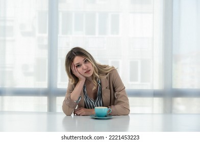 But First Coffee. Young Tired Business Woman In Formal Wear Sitting In The Office At Empty Desk With Cup Of Coffee. Female White Collar Worker, Freelancer Financial Expert Morning Routine.