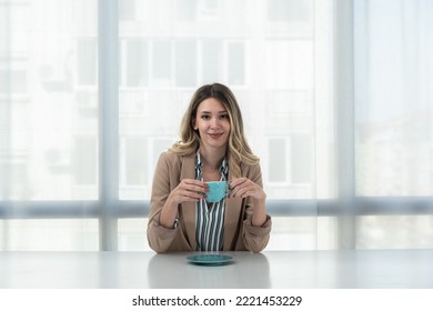 But First Coffee. Young Tired Business Woman In Formal Wear Sitting In The Office At Empty Desk With Cup Of Coffee. Female White Collar Worker, Freelancer Financial Expert Morning Routine.