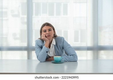 But First Coffee. Young Unhappy Tired Business Woman In Formal Wear Sitting In The Office At Empty Desk With Cup Of Coffee. Female White Collar Worker, Freelancer Financial Expert Morning Routine.