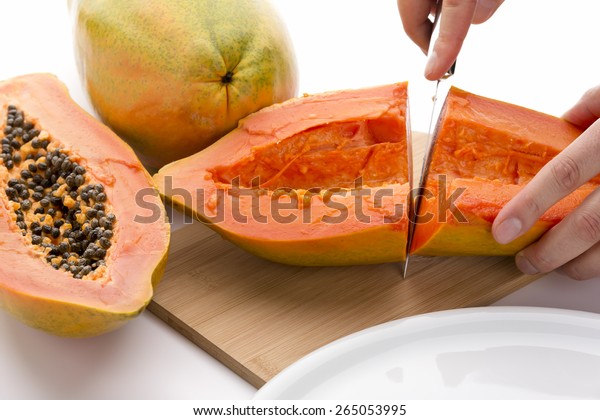First cut through a hollowed out half of a papaya.\
Finger tips of the left hand of a chef are fixing the fruit on a\
wooden cutting board, while his right is guiding a kitchen knife.\
Cutout. Close up.