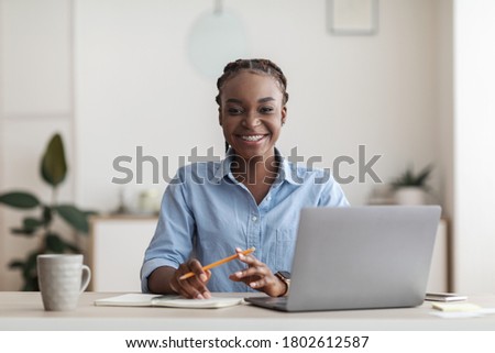 First Day In Office. Young Black Woman Trainee Sitting At Workplace At Desk With Laptop, Smiling At Camera