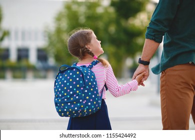first day at school. father leads a little child school girl in first grade