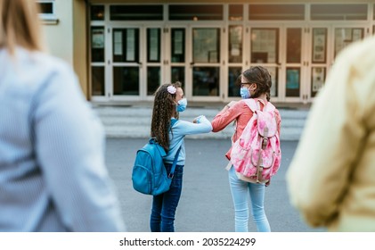 First Day At School. Girls With Face Masks Bumping Ellbows Because Of Coronavirus Pandemic.