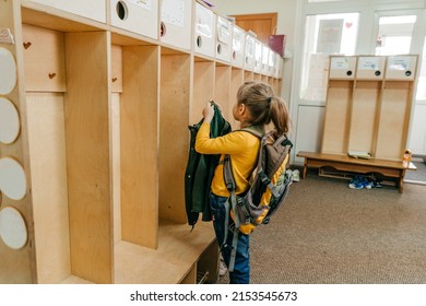 First Day At School Or Kindergarten. Little Girl With Backpack Hanging Her Jacket On A Hanger In A Wardrobe At School. Back To School Concept.