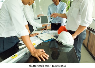 The First Engineering Team Working On The Construction Plan. They Stand At The Table Near The Blueprint. The Man Pointed To The IPad.