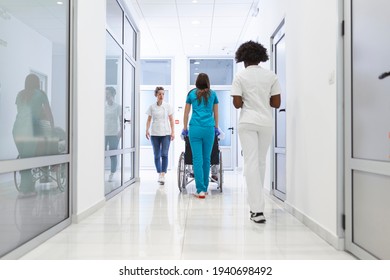 First Floor Of The Busy Hospital, Doctors, Nurses And Personnel Busy Working, Assistant Moves Elderly Man In The Wheelchair. New Modern Medical Hospital With Professional Staff.