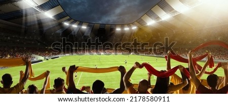 First game period. Back view of football, soccer fans cheering their team with colorful scarfs at crowded stadium at evening time. Concept of sport, cup, world, team, event, competition
