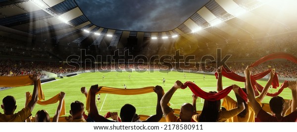 First game\
period. Back view of football, soccer fans cheering their team with\
colorful scarfs at crowded stadium at evening time. Concept of\
sport, cup, world, team, event,\
competition
