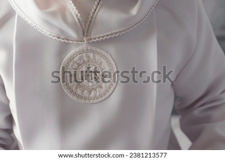 first Holy Communion. close-up of the IHS sign on the boy's communion apron. Boy's first communion outfit. An unrecognizable first communion child. White alba with the inscription IHS - detail. 