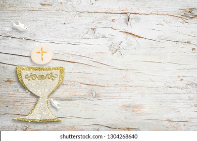 First Holy Communion invitations, silver and gold chalice and dove on white wooden background with empty space for text and photos