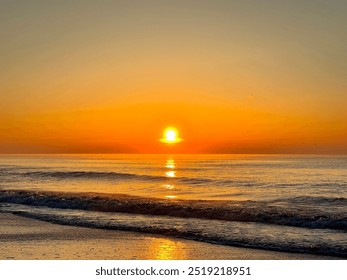 As the first light of dawn breaks over the horizon, a fiery orange sun rises from the azure waters of the ocean, painting the sky and waves with a breathtaking golden hue over Myrtle Beach, SC - Powered by Shutterstock