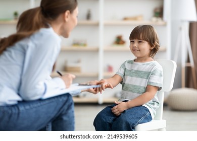 First meeting with patient. Friendly professional woman child psychologist greeting cute little boy, touching his hand and smiling at office