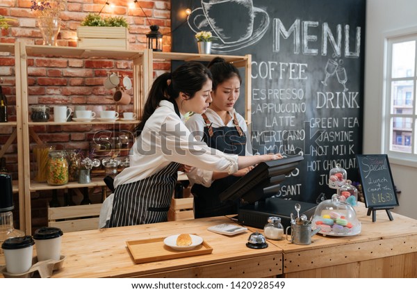 first part time job in summer concept. professional
barista teaching young girl new employee how to using tablet to
take customer order in cafe bar counter in coffee shop. coworkers
help each other
