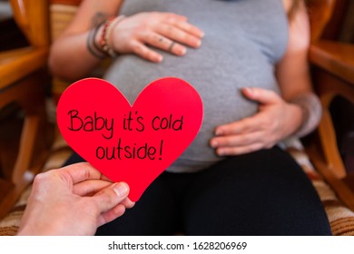 First Person Perspective Of Dad To Be Holding Message For Valentine Child, Baby Its Cold Outside, With Mom To Be Blurry In Background And Copy Space