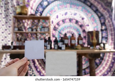 A First Person Perspective With Selective Focus Of A Person Holding A Blank White Label Against A Handicraft Stall Selling Organic Cosmetic Products