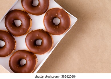 First Person Perspective Top Down View Of Six Chocolate And Cream Donuts In Open Box Over Brown Table With Copy Space