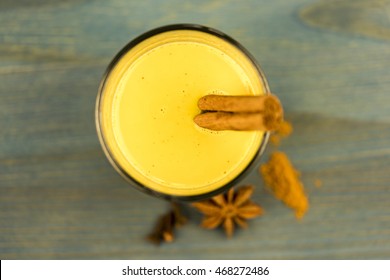 First person perspective top down view on turmeric latte with cinnamon sticks and anise herb on wooden table