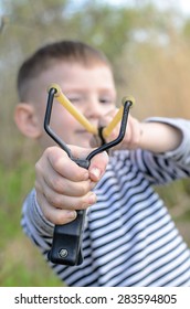 First Person Perspective Of Young Boy Holding Sling Shot, Pulling Rubber Strips Back In Anticipation Of Catapult Shot Across Lake