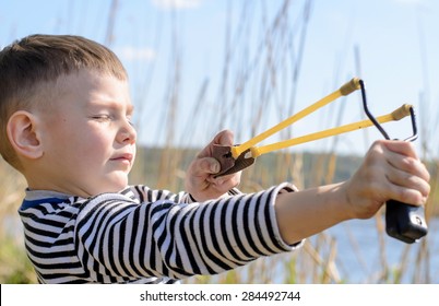 First Person Perspective Of Young Boy Holding Sling Shot, Pulling Rubber Strips Back In Anticipation Of Catapult Shot Across Lake