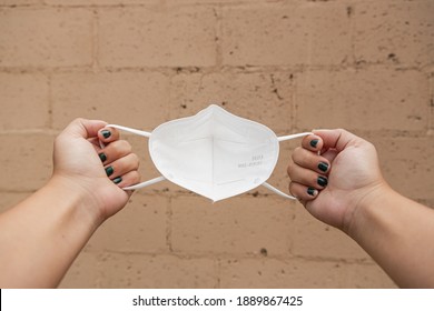 First Person Perspective Of A Young Latina Hands Holding A KN95 Mask Before Wearing  To Prevent Covid-19 With Wall In The Background. Health And Prevention Concept