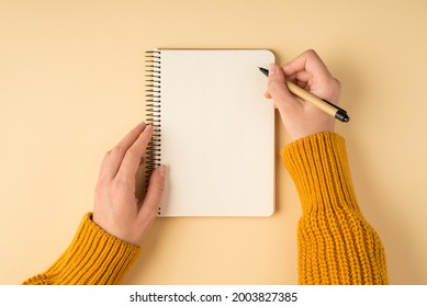 First person top view photo of female hands in yellow pullover writing in spiral notepad on isolated light orange background with copyspace