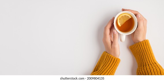 First person top view photo of female hands in yellow sweater touching white cup of tea with lemon slice on isolated white background with copyspace - Shutterstock ID 2009804135