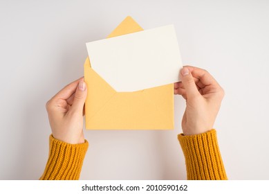 First person top view photo of female hands in yellow sweater holding open envelope with white card on isolated white background with blank space