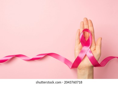 First person top view photo of female hand holding pink ribbon in palm symbol of breast cancer awareness on isolated pastel pink background with copyspace - Shutterstock ID 2043760718