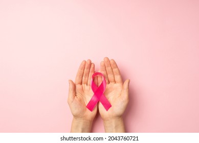 First person top view photo of girl's hands holding pink ribbon in palms symbol of breast cancer awareness on isolated pastel pink background with blank space - Shutterstock ID 2043760721