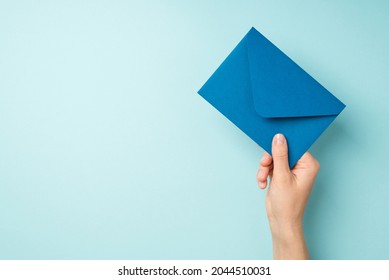 First person top view photo of hand holding closed blue envelope on isolated pastel blue background with copyspace