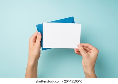 First person top view photo of hands holding blue envelope and white card on isolated pastel blue background with empty space