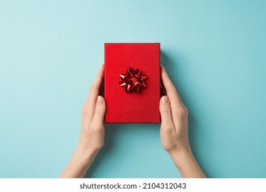 First person top view photo of valentine's day decorations young female hands holding red giftbox with red star bow on isolated pastel blue background with copyspace