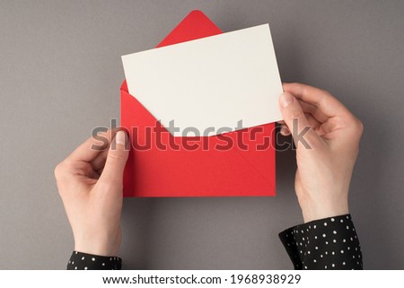 First person top view photo of female hands holding open red envelope with white card on isolated grey background with copyspace