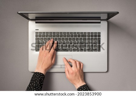 First person top view photo of hands using laptop touchpad and typing on keyboard on isolated grey background