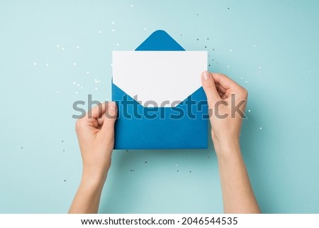 First person top view photo of hands holding open blue envelope with white card over sequins on isolated pastel blue background with empty space