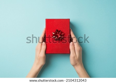 First person top view photo of valentine's day decorations young female hands holding red giftbox with red star bow on isolated pastel blue background with copyspace