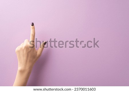 First person top view showcases fashionable young lady's hand, donning chic black nail polish, shaping choosing sign with her index finger. Purple background offers space for text or advertisements