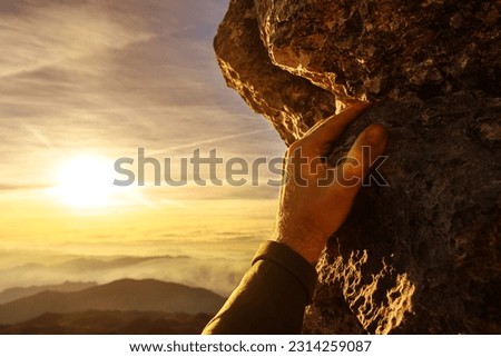 first person view of a climber's hand clinging to the rock of a mountain at sunset. Adventure and sport. risk sport.