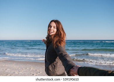 First Person View Of Man Holding Hand Of Smiling Woman In Warm Jacket On The Beach