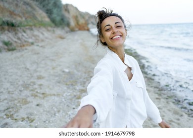 First person view portrait playful woman spontaneous smile to camera, girl holding boyfriends hand on beach, point of view
