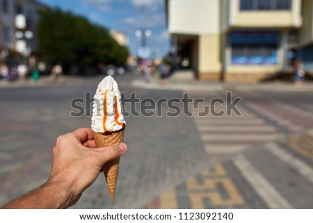 A first person view, a person walking along the road with an ice cream in his hands, shallow depth of field, vertical.