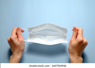 First person view of a woman holding face mask over blue textured table background. Protective raspiratory mask for spreading virus. Close up, copy space, top view, flat lay.