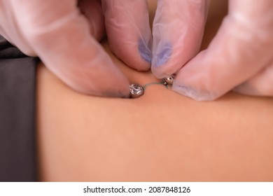 The first piercing. Dressing the earrings on the navel. Female piercing.