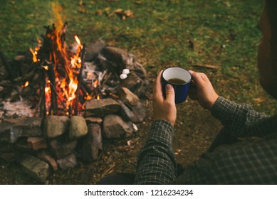 first point of view. man drinking tea in metal cup near camp fire. hiking